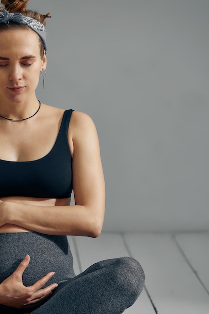 Young pregnant millennial woman sitting on the mat touches her belly after performing prenatal and meditation exercises at a yoga class Concept of life and maternity