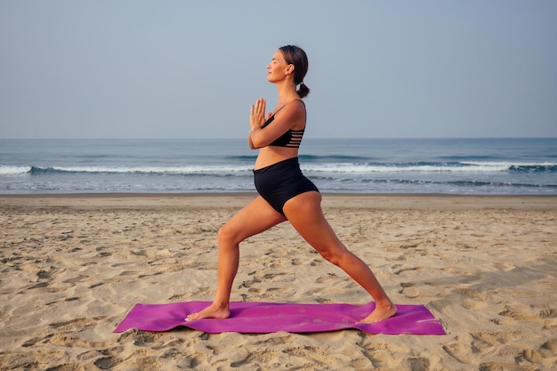 Young pregnant woman doing yoga exercises on the beach.