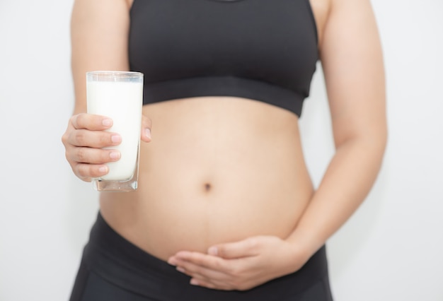 Young pregnant woman holding a glass of milk on right hand and touching her belly with care on left hand.