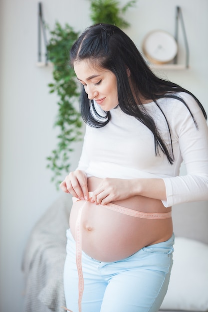 Young pregnant woman indoor. Lady measuring her round stomack. Beautiful woman expecting baby.