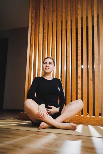 A young pregnant woman is doing sports while sitting on a mat Active way of life of a pregnant woman Sports for pregnant women