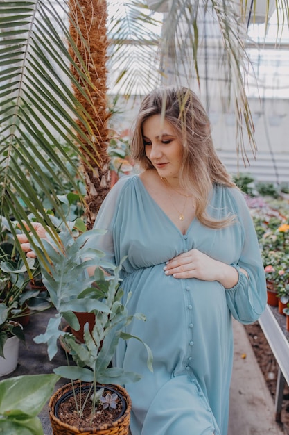 A young pregnant woman is watering flowers in a greenhouse Spring at home and winter outside the window