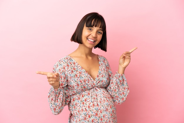 Young pregnant woman over isolated pink background pointing finger to the laterals and happy