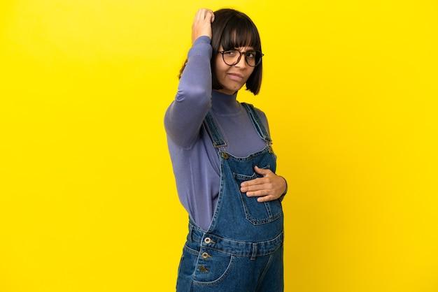 Young pregnant woman over isolated yellow background having doubts while scratching head