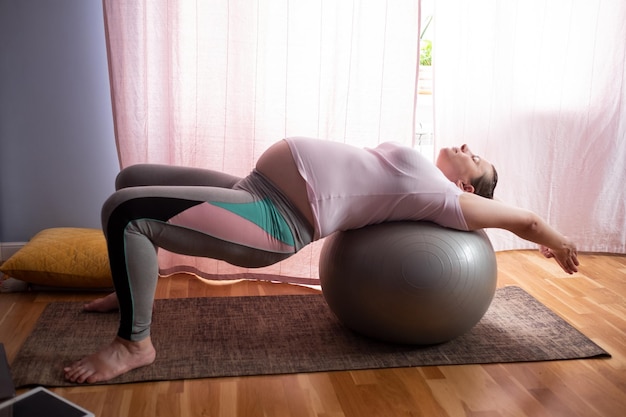 Young pregnant woman practices yoga at home