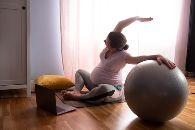 Young pregnant woman practices yoga at home