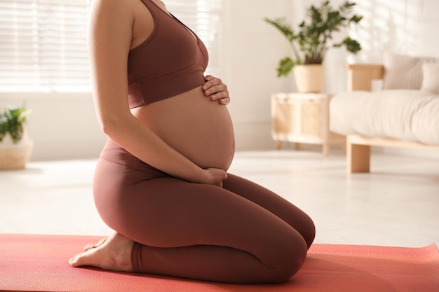 Young pregnant woman practicing yoga at home closeup