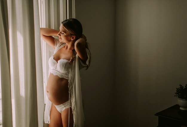 Young pregnant woman standing by the window