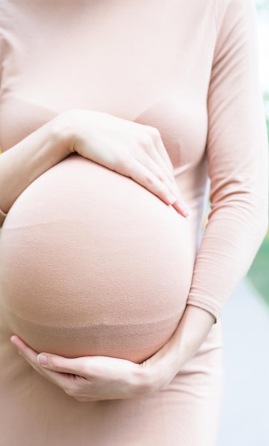 Young Pregnant Woman Standing Outdoors in City Park and Holding Her Belly Motherhood Pregnancy People and Expectation Concept