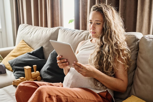 Young pregnant woman with digital tablet watching blog for future mothers