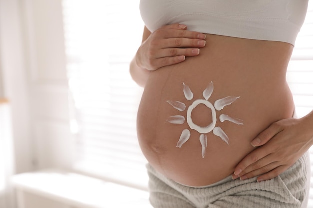 Young pregnant woman with sun protection cream on belly indoors closeup Space for text