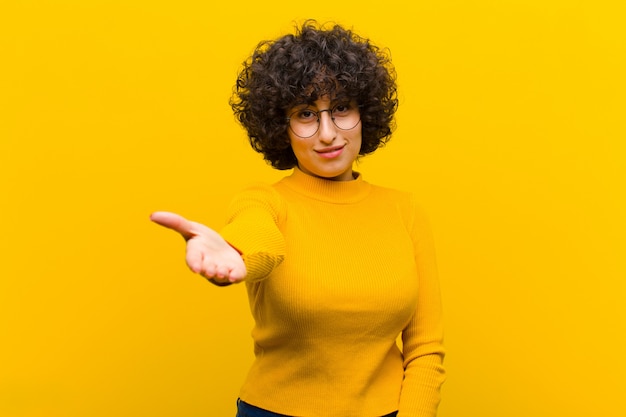 Young pretty afro woman smiling, looking happy, confident and friendly, offering a handshake to close a deal, cooperating