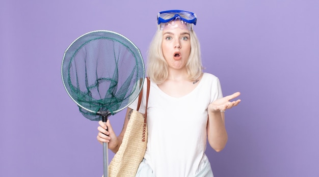 Young pretty albino woman amazed, shocked and astonished with an unbelievable surprise with goggles and a fishing net