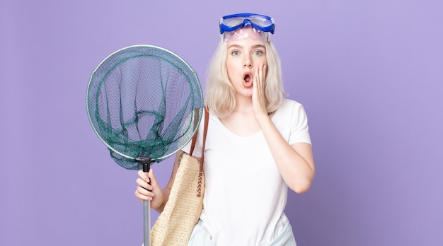 Young pretty albino woman feeling shocked and scared with goggles and a fishing net