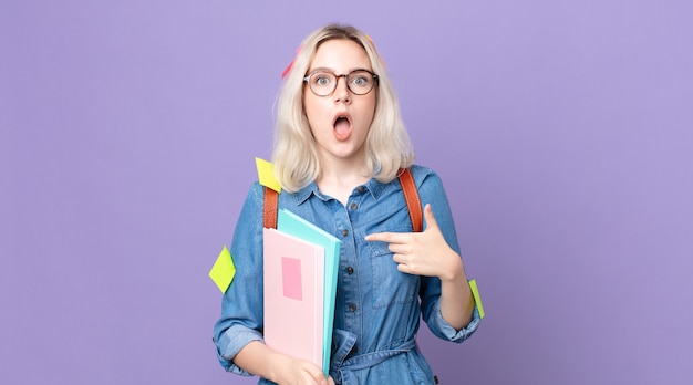 Young pretty albino woman looking shocked and surprised with mouth wide open, pointing to self. student concept