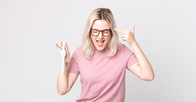 Photo young pretty albino woman looking unhappy and stressed, suicide gesture making gun sign holding a watch clock