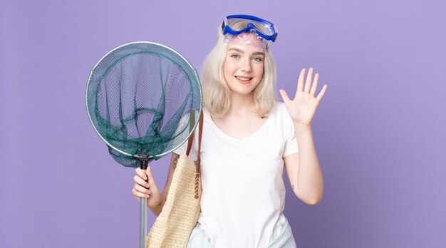 Young pretty albino woman smiling and looking friendly, showing number five with goggles and a fishing net