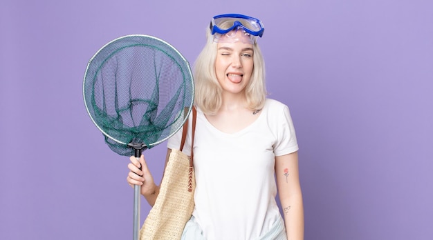 Young pretty albino woman with cheerful and rebellious attitude, joking and sticking tongue out with goggles and a fishing net