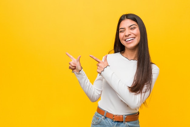 Young pretty arab woman against a yellow background pointing with forefingers to a copy space, expressing excitement and desire.