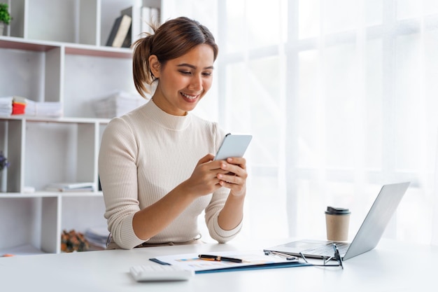 Young Pretty Asian businesswoman using smartphone when working at desk in office