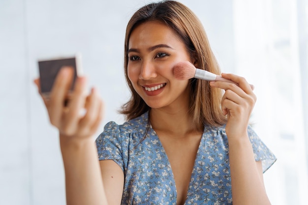 Young pretty Asian woman beauty vlogger doing a makeup tutorial when sitting at desk in living room