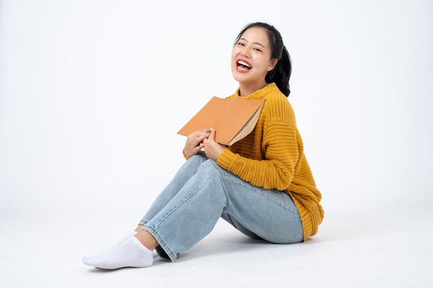 Young pretty Asian woman in casual clothes sits on an isolated studio white background with a book