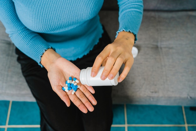 Young Pretty Asian woman holding medicine pills when sitting on couch