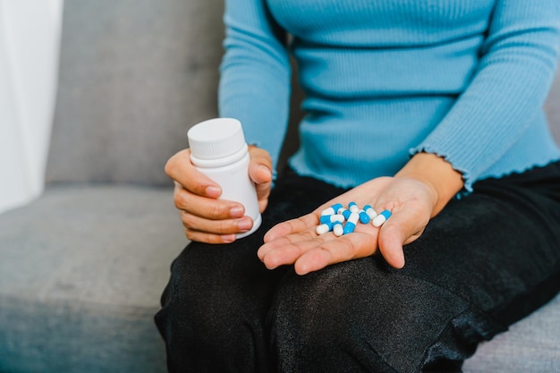 Young Pretty Asian woman holding medicine pills when sitting on couch