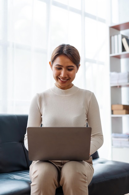 Young pretty Asian woman using laptop when sitting on sofa in living room