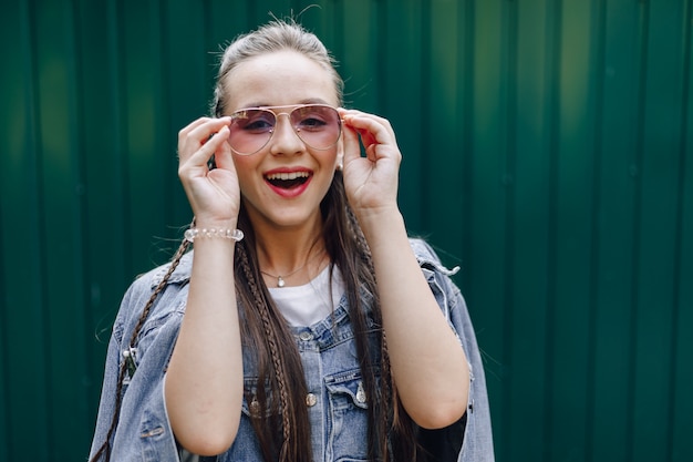 Young pretty attractive girl in denim clothes in glasses on a simple dark green background with place for text.