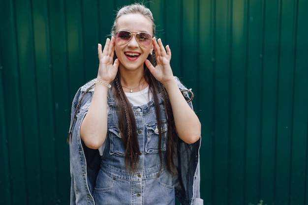 Young pretty attractive girl in denim clothes in glasses on a simple dark green background with place for text.