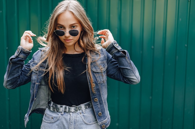 Young pretty attractive girl in denim clothes in glasses on a simple dark green background with place for text.