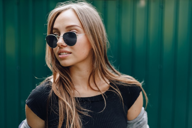 Young pretty attractive girl in denim clothes in glasses on a simple dark green background with place for text.