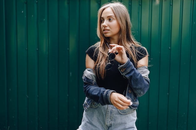 Young pretty attractive girl in denim clothes in glasses on a simple dark green background with place for text.