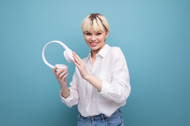 Young pretty blond student woman dressed in a white blouse listens to her favorite music in