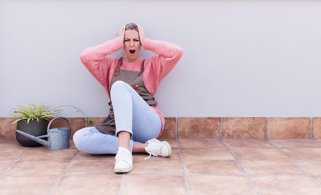 Young pretty blonde gardener woman sitting on the floor with a copy space to the side