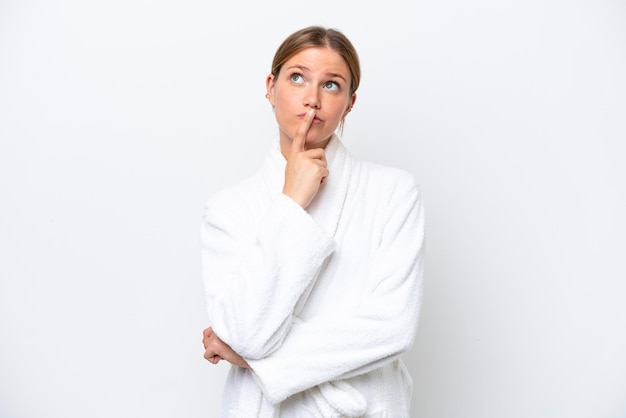 Young pretty blonde woman in bathrobe isolated on white background having doubts while looking up