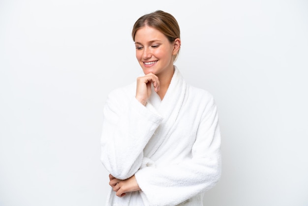 Young pretty blonde woman in bathrobe isolated on white background looking to the side and smiling