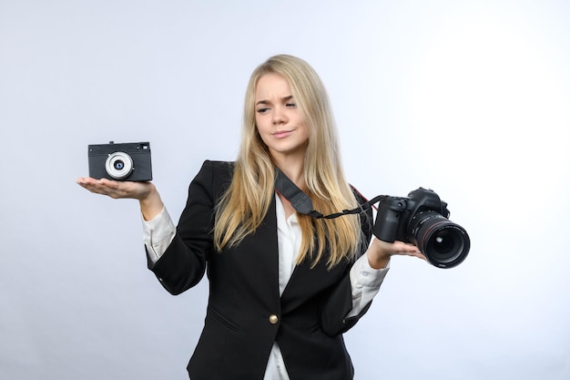 Young pretty blonde woman compares retro film camera and modern DSLR cameras on white background