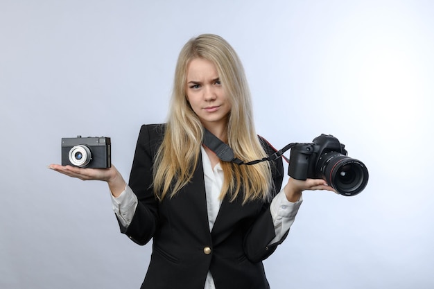 Young pretty blonde woman compares retro film camera and modern DSLR cameras on white background