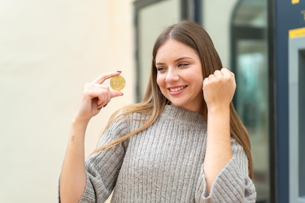 Young pretty blonde woman holding a Bitcoin at outdoors celebrating a victory