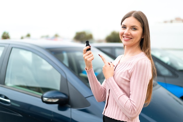 Young pretty blonde woman holding car keys at outdoors and pointing it