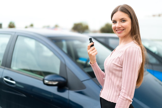 Young pretty blonde woman holding car keys at outdoors smiling a lot