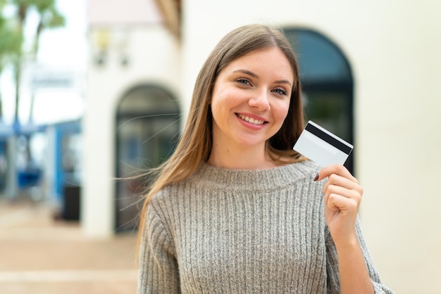 Young pretty blonde woman holding a credit card at outdoors smiling a lot