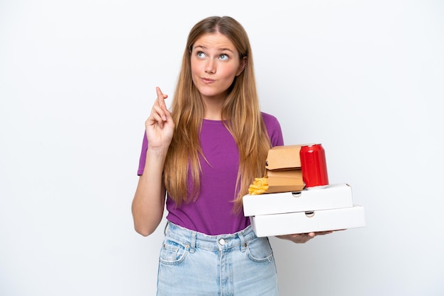 Young pretty blonde woman holding fast food isolated on white background with fingers crossing and wishing the best