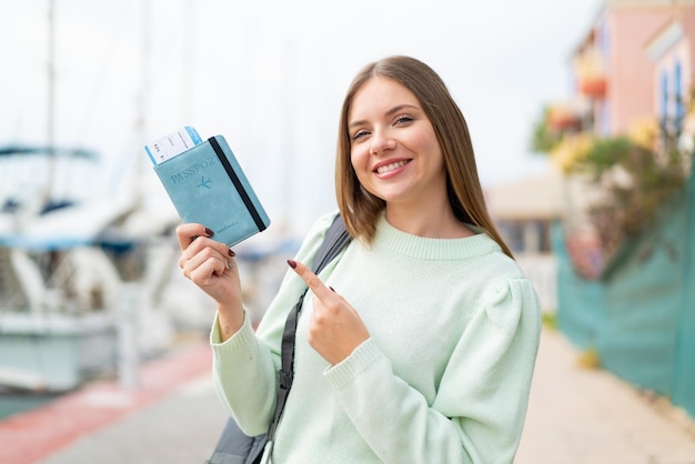 Young pretty blonde woman holding a passport at outdoors and pointing it