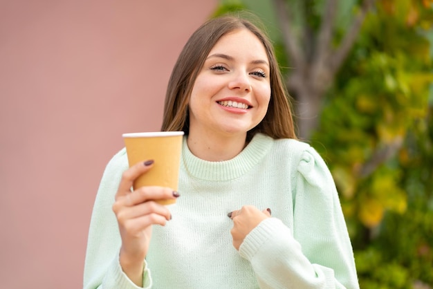 Young pretty blonde woman holding a take away coffee at outdoors with surprise facial expression