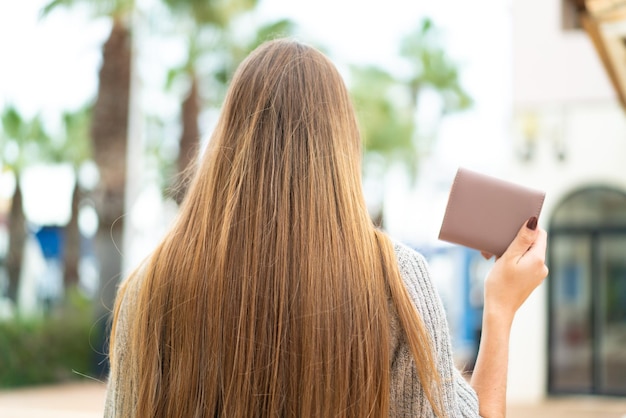 Young pretty blonde woman holding a wallet at outdoors in back position