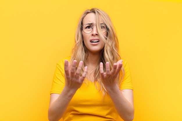 Young pretty blonde woman looking desperate and frustrated, stressed, unhappy and annoyed, shouting and screaming against flat color wall