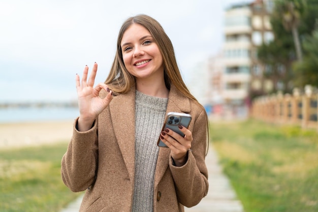 Young pretty blonde woman using mobile phone and doing OK sign